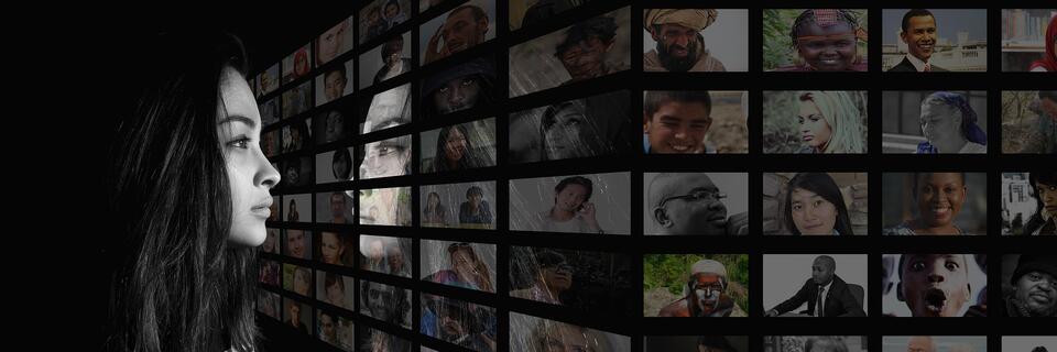 #vorbild. Eine junge Frau betrachtet viele Fotos mit Portraits, die an einer Wand aufgehängt sind.